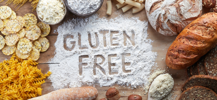 Rozsypana mąka na stole, w której napisano "Gluten free", obok makarony, mąki, chleby